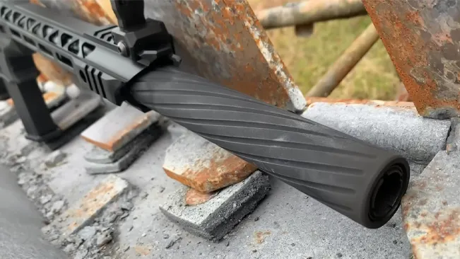 A close-up of a fluted barrel on a black rifle resting on a concrete surface