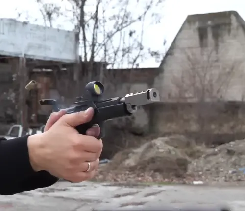 A person's hand firing a CZ 75 TS Czechmate pistol, capturing the ejected casing in motion with an urban decay background.