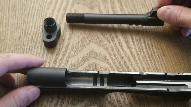 Hands disassembling the barrel and compensator from the slide of a CZ 75 TS Czechmate, laid out on a wooden table for maintenance.