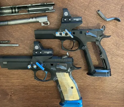Two disassembled CZ 75 TS Czechmate pistols with blue and gold grips, optical sights, and various components laid out on a wooden table.