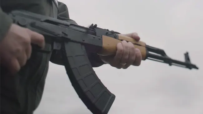 Close-up of hands holding a Century Arms WASR-10 rifle with wooden foregrip and black magazine