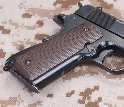 Colt 1911 pistol with brown grips lying on a camouflaged background