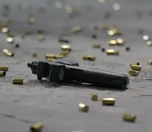 A black semi-automatic pistol lying on the ground surrounded by scattered brass bullet casings.