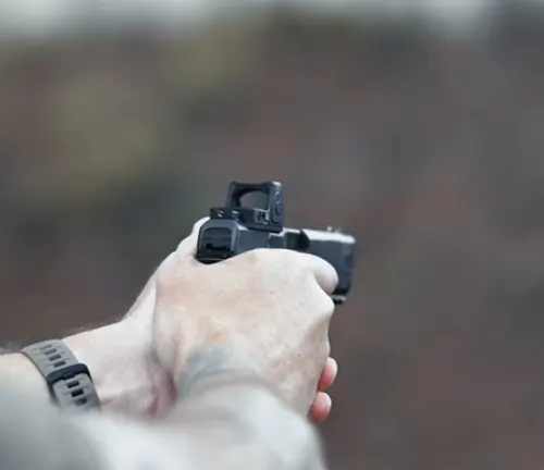First-person view of hands holding a black semi-automatic pistol with a reflex sight, aiming down the sights.
