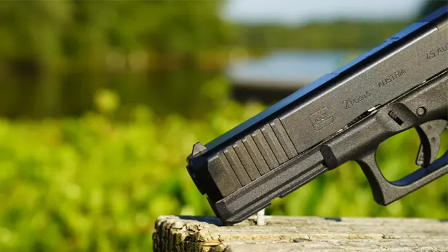 Close-up of a Glock 17 pistol resting on a weathered wooden surface, with the slide inscription visible, set against a vibrant green foliage background.