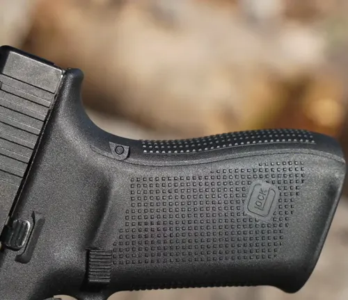 Close-up of the textured grip and magazine release of a Glock pistol, with a blurred background providing a bokeh effect.