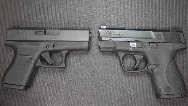Glock 43 and S&W M&P Shield pistols laid out for comparison on grey fabric.
