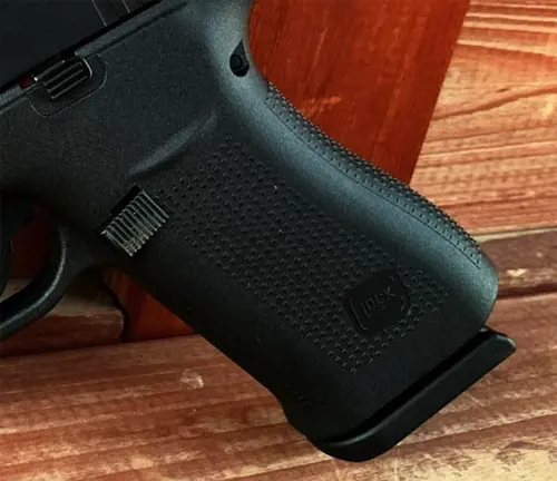Close-up of the grip on a Glock 48 showing the textured polymer surface and the Glock logo, with a wood background.