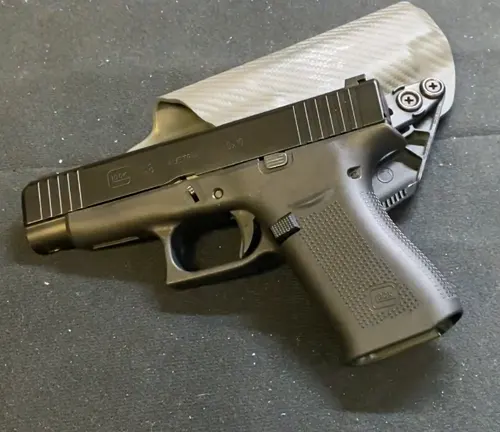 A Glock 48 pistol with a black frame and silver slide, equipped with a rear slide-mounted red dot sight, lying on a grey textured surface.