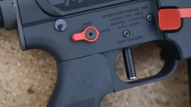 Close-up of a rifle's lower receiver showing safety selector, trigger, and manufacturer's information.