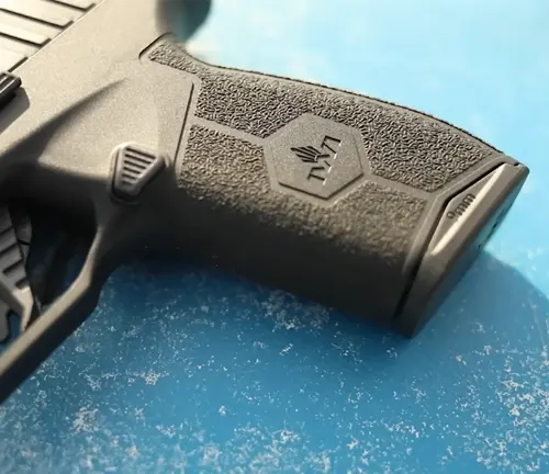 Close-up of the textured grip and backstrap of an IWI Masada Slim pistol with the IWI logo, showcasing the ergonomic design and stippling for enhanced handling.