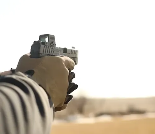 First-person perspective of a shooter aiming an IWI Masada Slim pistol with a mounted red dot sight, with a focus on the hands and firearm against a blurred background.