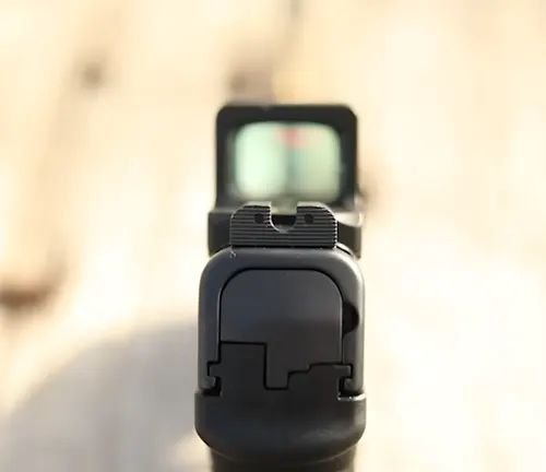 Rear view of an IWI Masada Slim pistol focusing on the rear sight and a mounted red dot optic, with a blurred target in the background.
