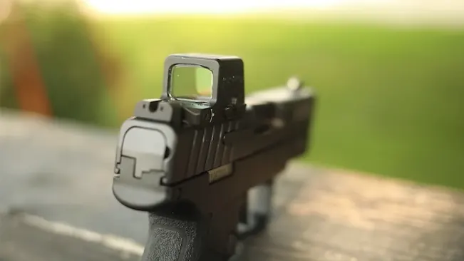 Rear view of an IWI Masada Slim pistol focused on the mounted red dot sight, set against a soft-focus background of greenery.