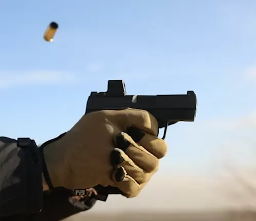 A gloved hand firing an IWI Masada Slim pistol, with a casing mid-ejection in a clear sky background.