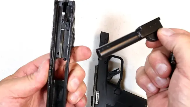 Hands performing maintenance on the disassembled slide and barrel of an IWI Masada Slim pistol against a white background.