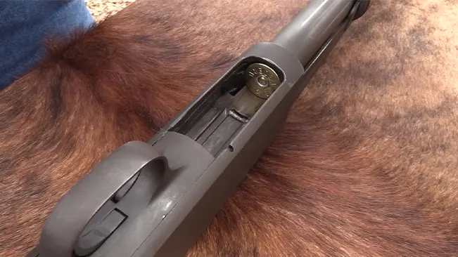 Overhead close-up of an Ithaca Model 37 shotgun showing a loaded round in the chamber, against a fur backdrop