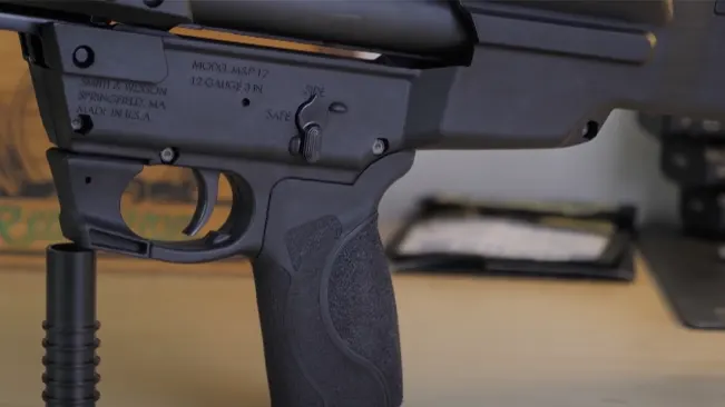 Close-up of the trigger area of an S&W M&P 12 shotgun, displaying the model and safety details.