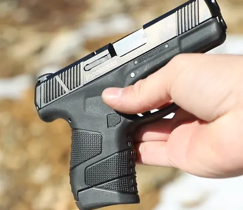 A hand gripping a Mossberg MC1SC pistol with the magazine ejected, showcasing the clear chamber indicator and textured grip design.