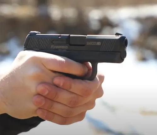 A Mossberg MC1SC pistol aimed directly at the camera, held securely in a two-handed grip, with a blurred background.