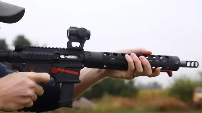 Person holding a modern sporting rifle with a red dot sight and customized parts, outdoors.