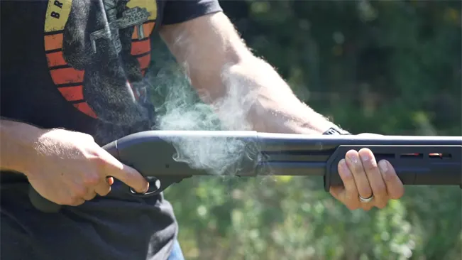 Person holding a shotgun with smoke emanating from the barrel after firing.