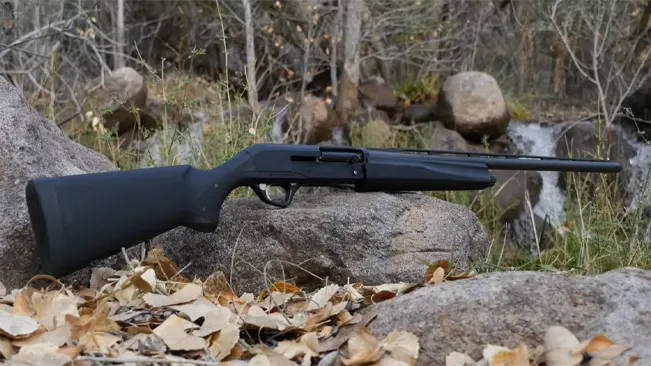 Versa Max Tactical shotgun with a synthetic stock lying on rocks among fallen leaves in a natural setting