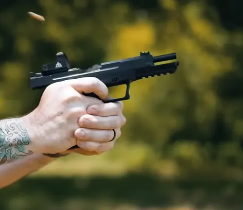 A person's tattooed hand firing a Ruger 5.7 pistol with a mounted reflex sight, casings being ejected, against a blurred natural background.