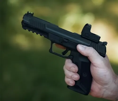 A close-up of a Ruger 5.7 pistol being held in a person's hand, with a mounted optic sight, against a defocused green background.