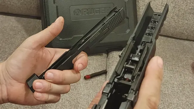 Hands performing maintenance on a disassembled Ruger American Competition pistol, holding the slide and barrel with a Ruger-branded case and a disassembled magazine in the background.