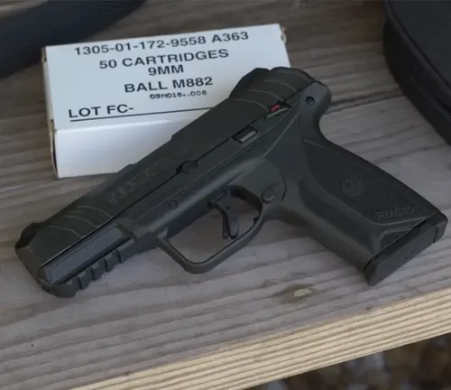 A Ruger Security-9 pistol displayed on a wooden surface next to a box of 9mm cartridges, with a focus on the gun's black polymer frame and visible red-dot safety indicator.