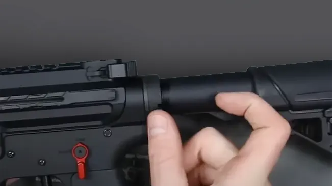 Close-up of hands adjusting the collapsible stock on a black rifle where the spring system is placed