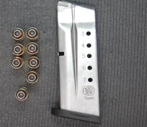 S&W Shield 9mm Pistol magazine alongside eight  9mm bullets on a grey background.