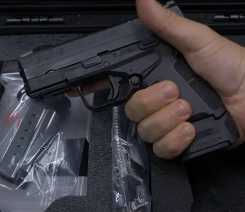 Hand gripping a black Springfield XD-S pistol over a case with spare magazines