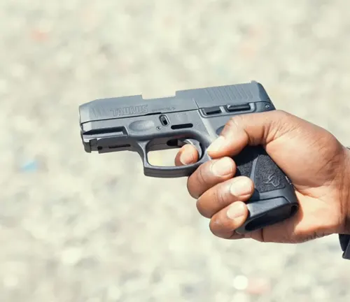 A person's hand holding a Taurus G3C semi-automatic pistol with a focus on the firearm against a blurred background, emphasizing the pistol's compact frame and textured grip.