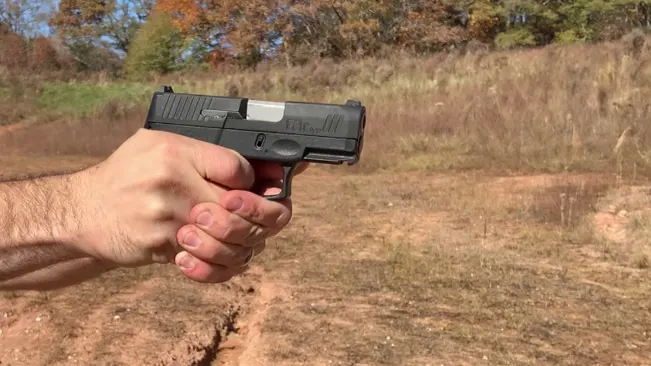 A Taurus G3C pistol is held steadily in a shooter's hand, ready to fire, with a clear view of the slide and barrel against an autumn-colored outdoor backdrop
