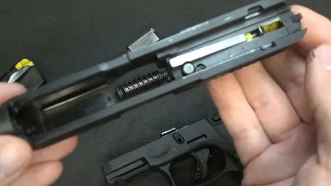 A close-up view of a disassembled Taurus G3C pistol slide in a person's hands, showing the barrel, recoil spring, and internal mechanisms, with the frame of the gun blurred in the background.