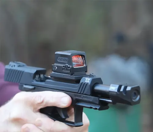 A Taurus TX22 Competition SCR pistol with a red dot sight held in a shooter's hands, with a blurred background emphasizing the firearm in focus.