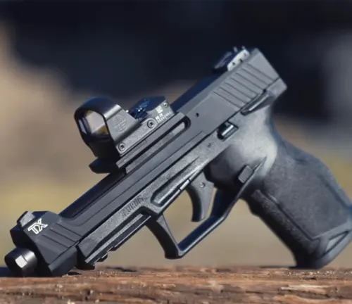 A Taurus TX22 Competition SCR pistol resting on a wooden surface with a mounted reflex sight, in a clear focus with a blurred natural backdrop.