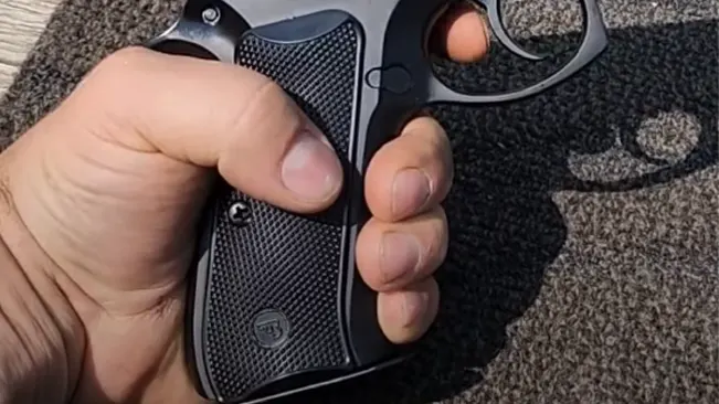 A close-up image of a person's hand gripping the textured black handle of a handgun, with fingers in position as if ready to fire.