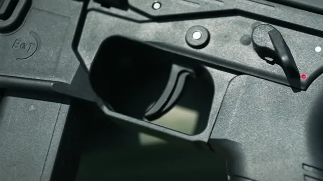 Close-up view of the magazine well and trigger of a black firearm, highlighting the internal mechanism and red safety indicator.