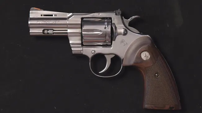 Colt Python revolver with a 3-inch barrel and wooden grips on a dark surface.