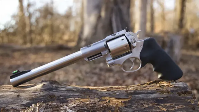 Ruger Super Redhawk revolver with a long barrel, resting on a log.