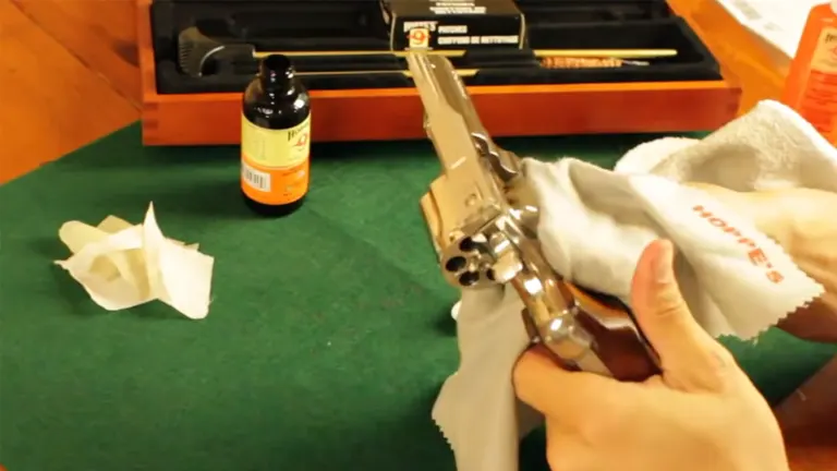 A hand cleaning a Smith & Wesson 627 revolver on a green mat with cleaning supplies in the background.