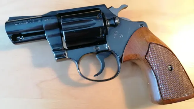 Colt Detective Special revolver with a blue finish and checkered wooden grip on a light background.