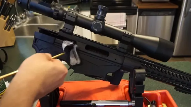Person cleaning a Ruger Precision Rifle with a scope mounted on top, using a cloth and a cleaning rod