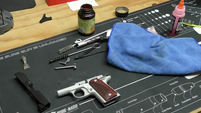 Disassembled Kimber Micro 9 pistol on a cleaning mat with various maintenance tools and supplies around.