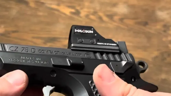 A hand holding a CZ-75 PCR compact pistol equipped with a Holosun red dot sight.