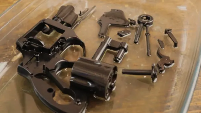 Disassembled parts of an Astra 680 revolver laid out on a glass surface.