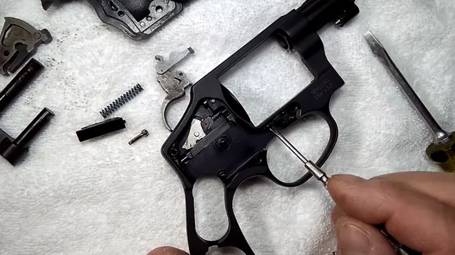 A hand disassembling the frame of a Smith & Wesson J-Frame 340 PD revolver, with parts laid out on a white towel.